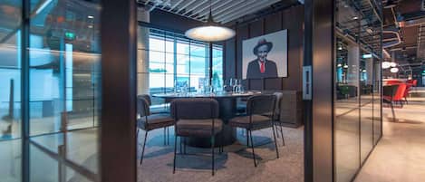A modern office space with a round table, chairs, and a large window.