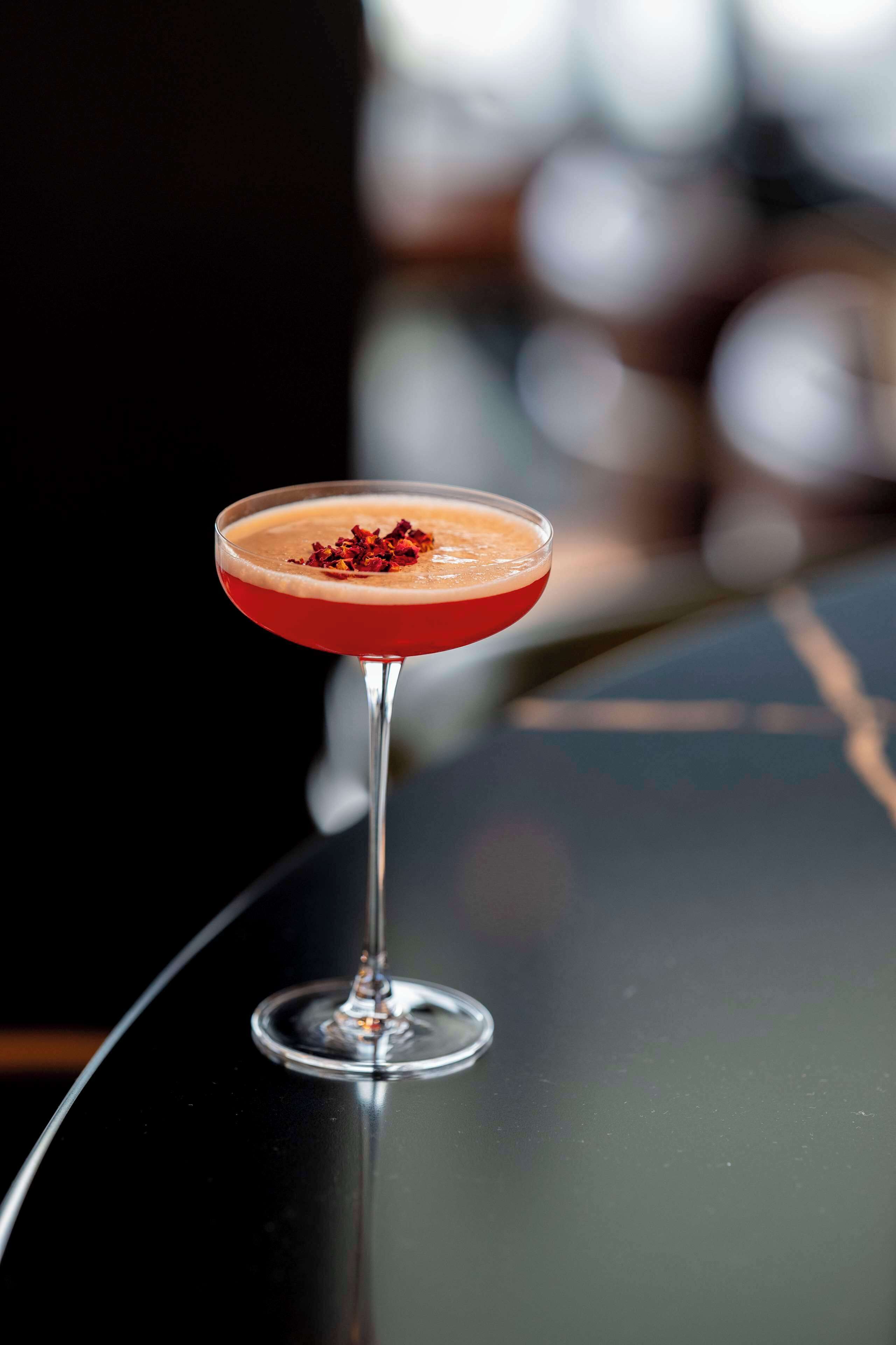 A cocktail in a martini glass on a reflective surface.