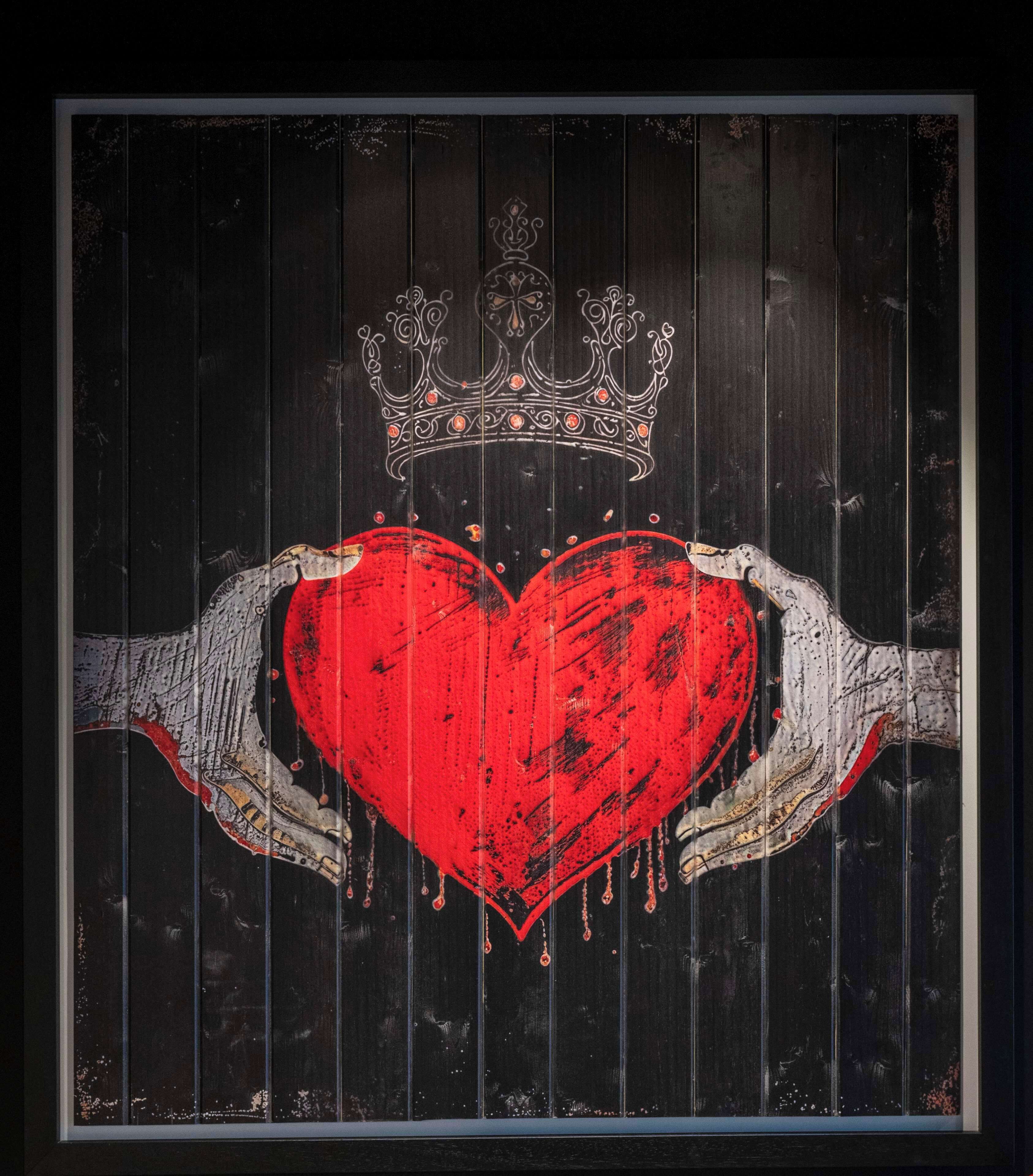 A framed artwork of a heart with a crown on a wooden background.