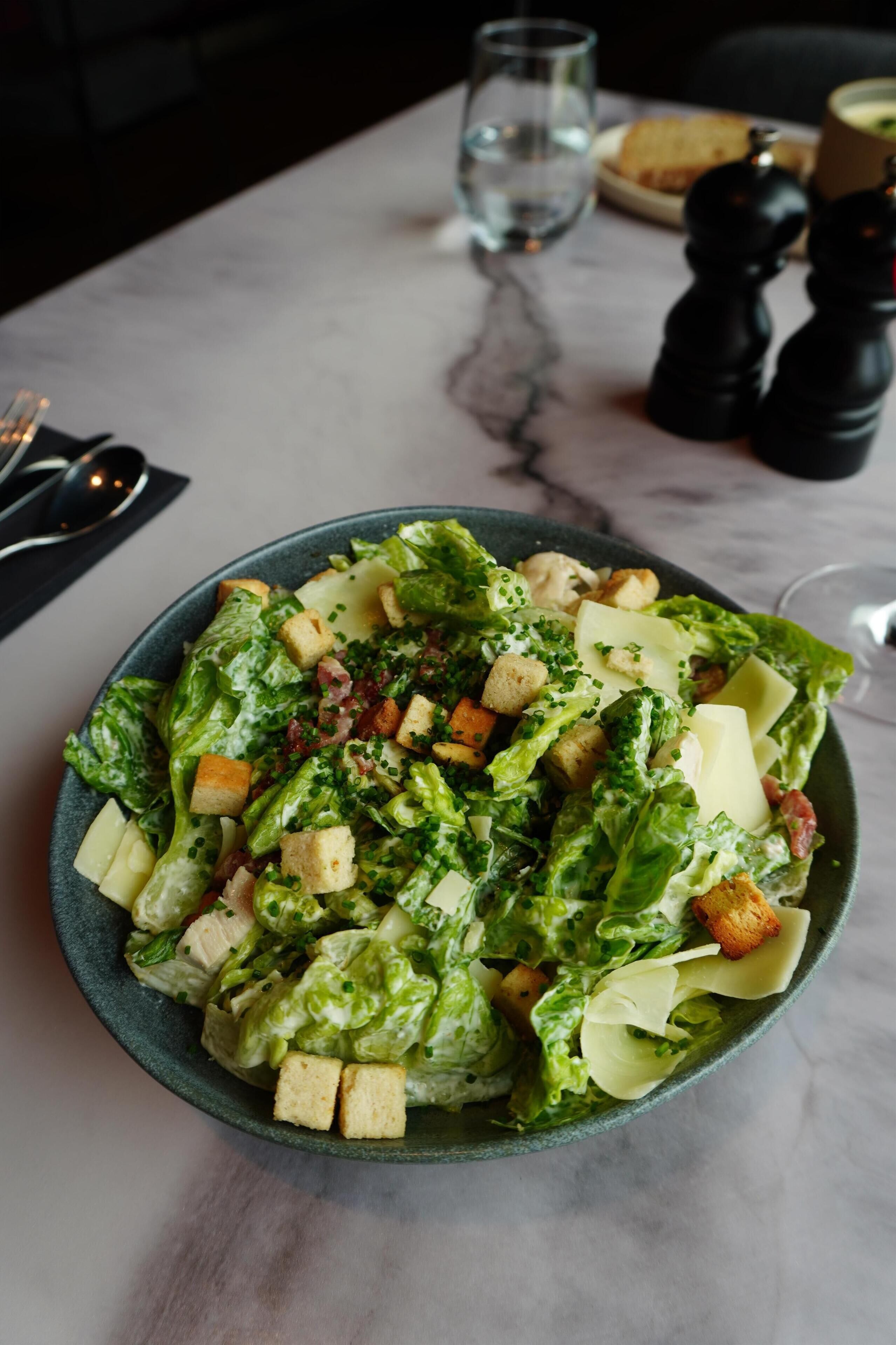 Uma salada Caesar numa taça, com croutons e queijo, sobre uma mesa de mármore.