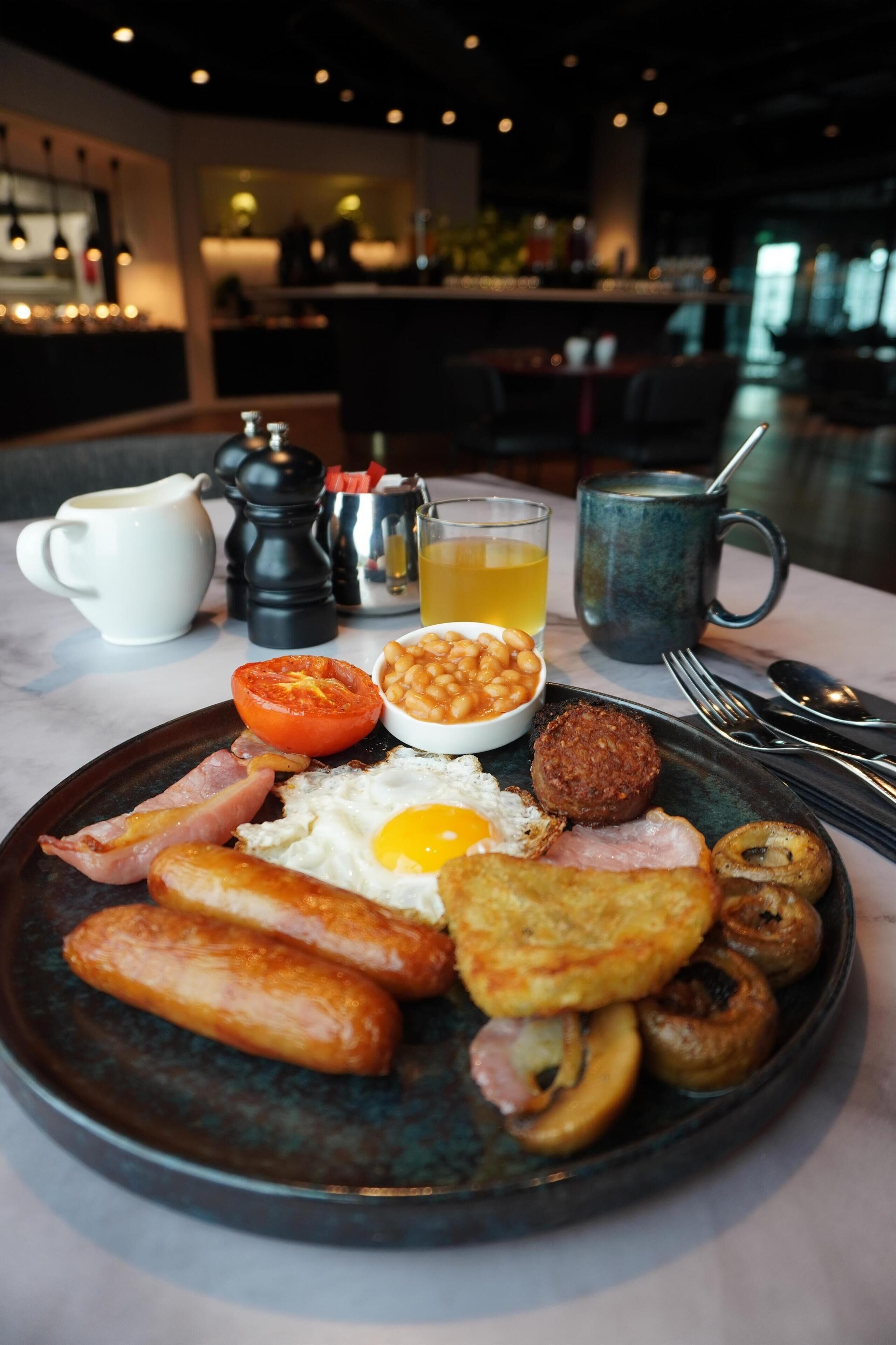 A breakfast plate with eggs, bacon, sausages, mushrooms, and beans.