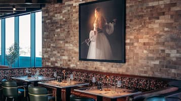 A restaurant with a brick wall, wooden ceiling beams, and a large framed portrait. Tables are set with chairs and candles.