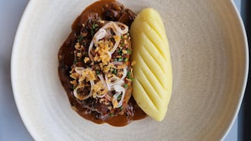 A plate with a meat dish, onions, and a side of mashed potatoes.