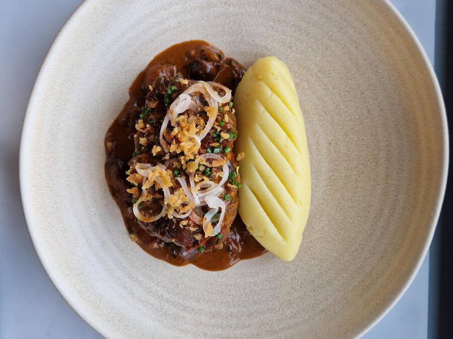Une assiette contenant un plat de viande, des oignons et une portion de purée de pommes de terre.