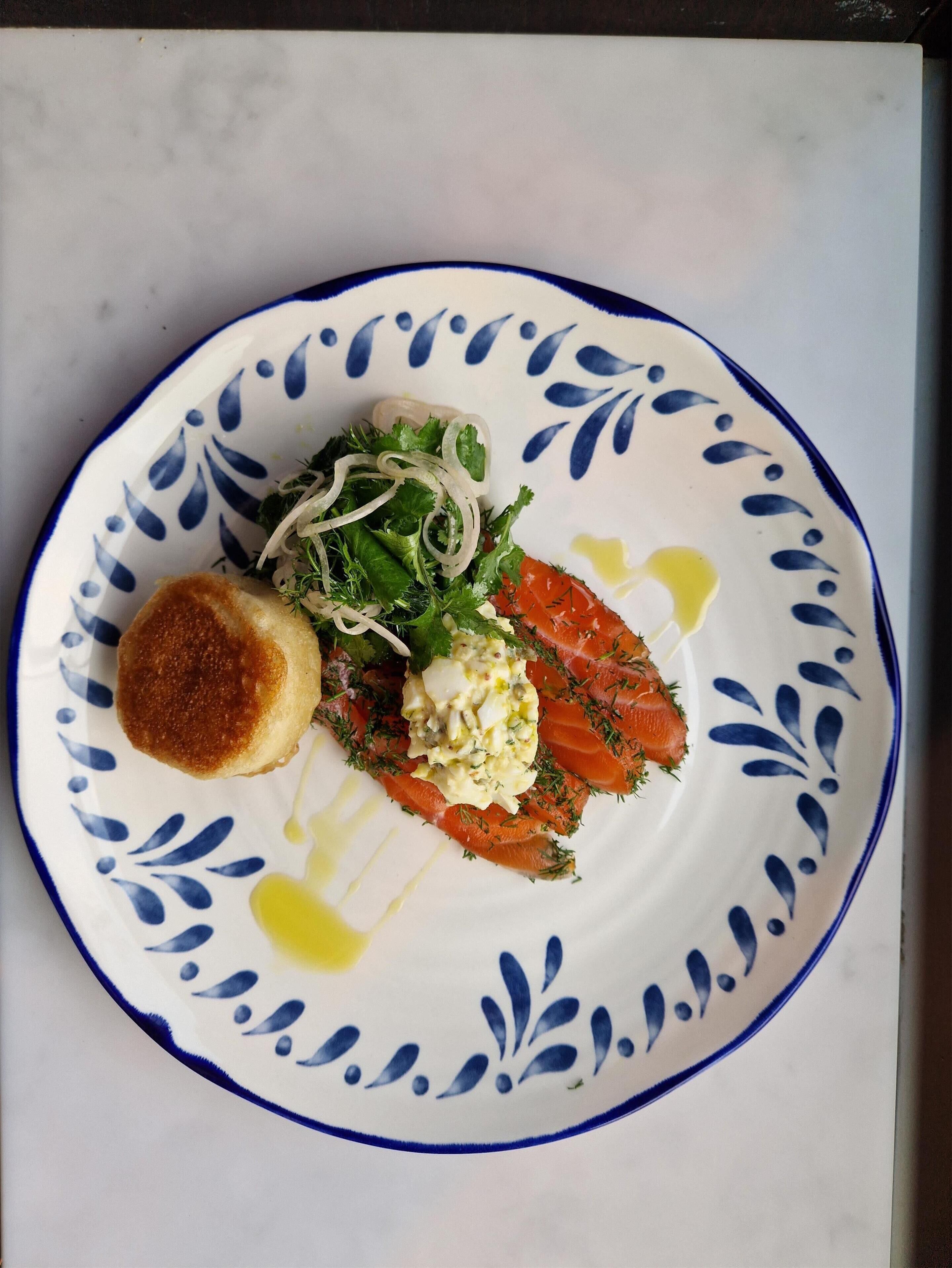 A plate with a piece of salmon, a small round item, and a salad with greens and onions.