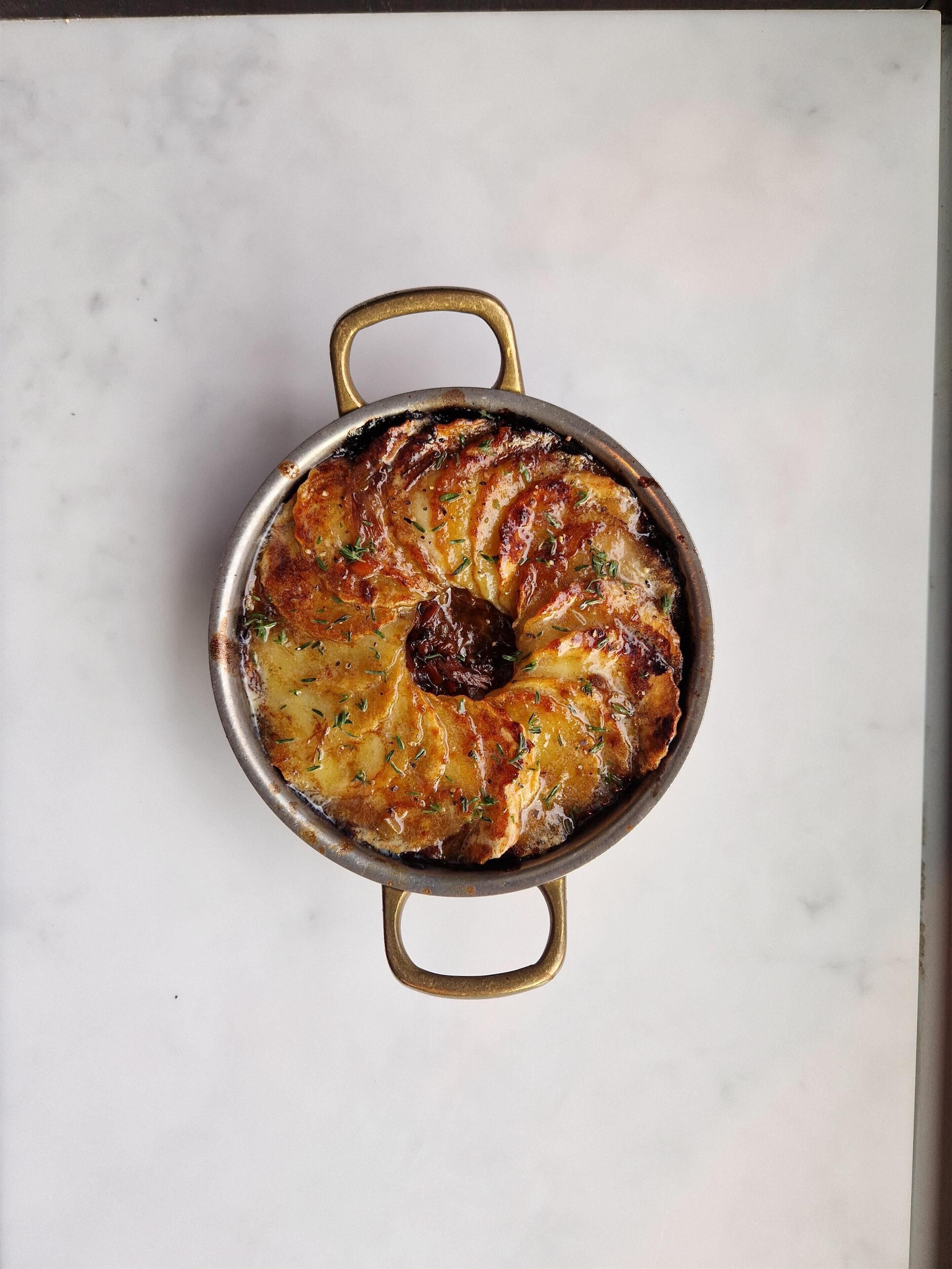 A round baking dish with handles, containing a baked dish with a golden-brown crust and herbs, placed on a white surface.