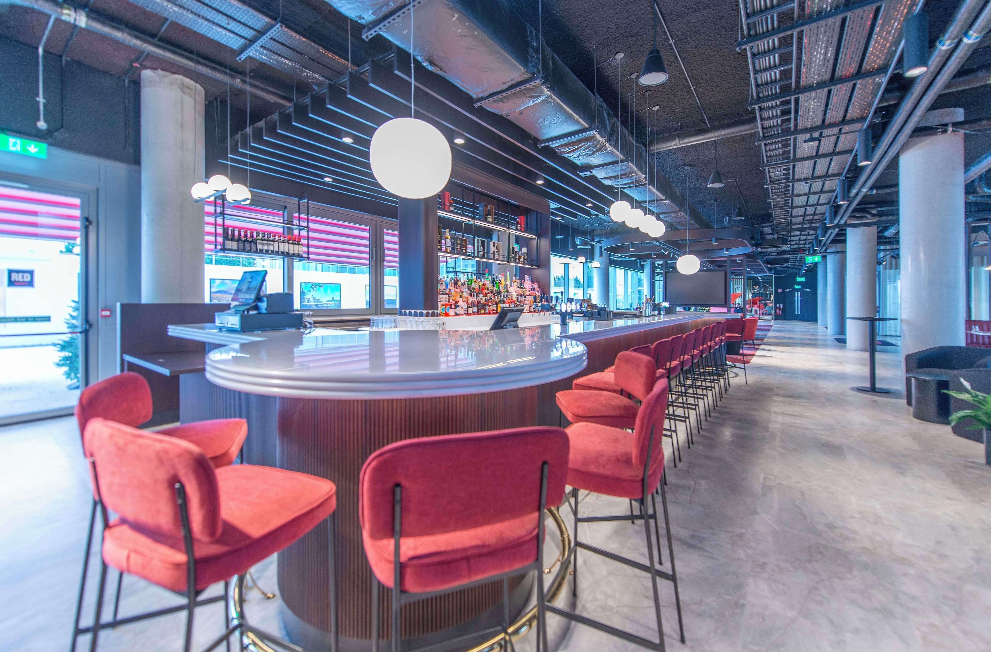 A modern bar area with a long counter, red bar stools, and a variety of bottles.