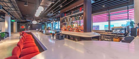 Zona de bar moderna con una barra larga, asientos rojos y una estantería repleta de licores.
