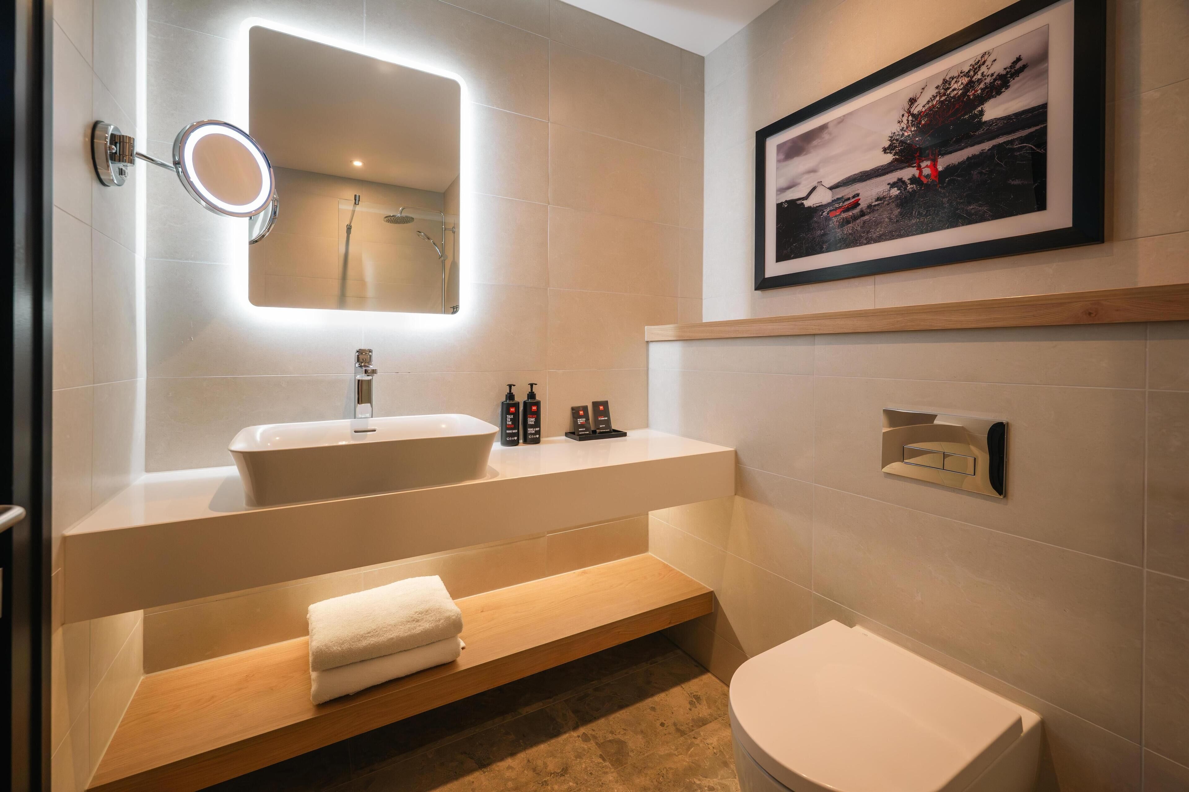 A modern bathroom with a large mirror, a sink, and a toilet.