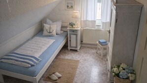 Un dormitori amb llit, taulella de nit, aparador i finestra amb cortines.