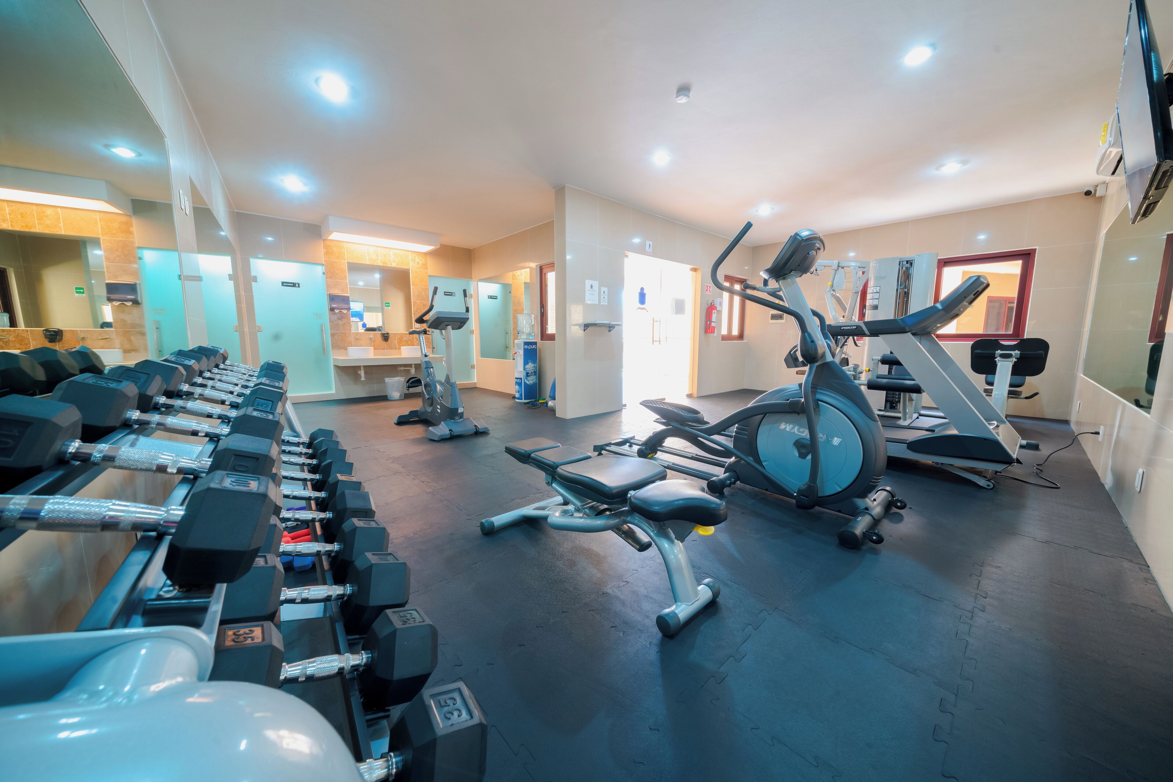Un gimnasio con diverso equipo de ejercicio, incluyendo mancuernas, cintas de correr y bicicletas estáticas.