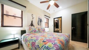 A bedroom with a large bed, a nightstand, a ceiling fan, and a door. - Surf 301 - Luxury Oceanview Beachfront (Playa del Carmen)