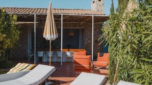 A sunlit outdoor lounge area with lounge chairs and a table, surrounded by stone walls and greenery. - Maison St Rémy Centre Piscine Chauffée et Hammam (Saint-Rémy-de-Provence)