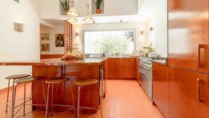 A modern kitchen with a central island, bar stools, wooden cabinets, and pendant lighting. - Maison St Rémy Centre Piscine Chauffée et Hammam (Saint-Rémy-de-Provence)