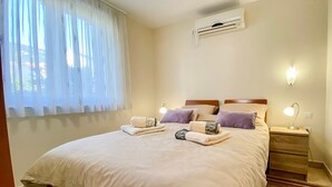 A neatly made bed with towels, a bedside lamp, and a nightstand in a room with a window and an air conditioning unit. - Ferienwohnung Maya Lorena (Baska)