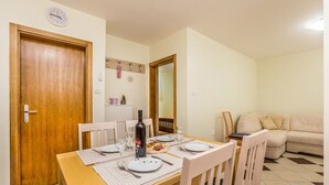 A dining area with a wooden table set for four, a wine bottle, and a mirror reflecting the room. - Ferienwohnung Maya Lorena (Baska)