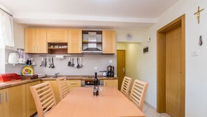 A compact kitchen with wooden cabinets, a dining table with chairs, and a coffee machine. - Ferienwohnung Maya Lorena (Baska)