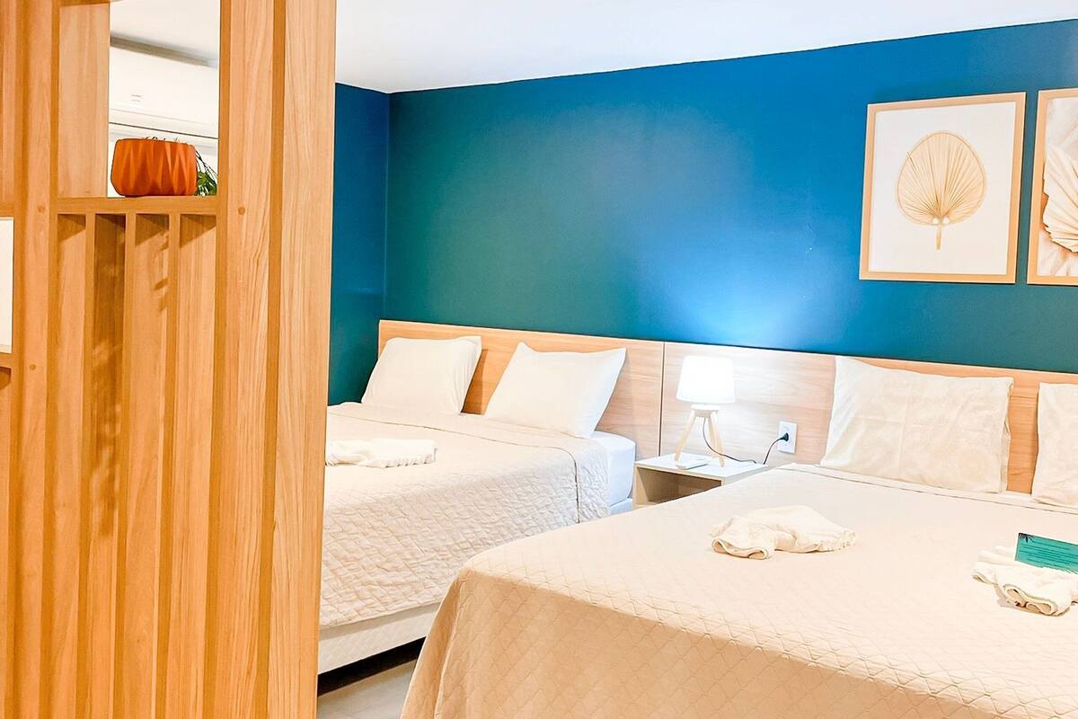 Une chambre d’hôtel avec deux lits, une cloison en bois et un mur bleu orné de tableaux encadrés.