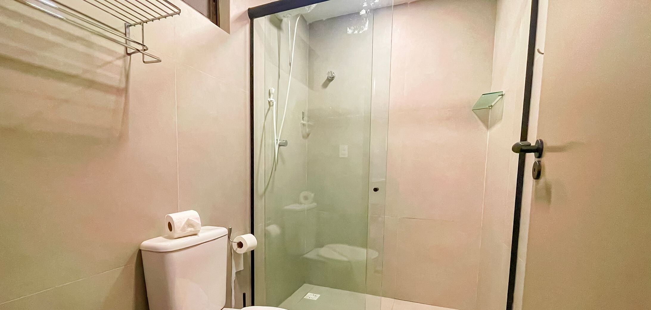 Um chuveiro fechado com porta de vidro, vaso sanitário e suporte para toalhas.