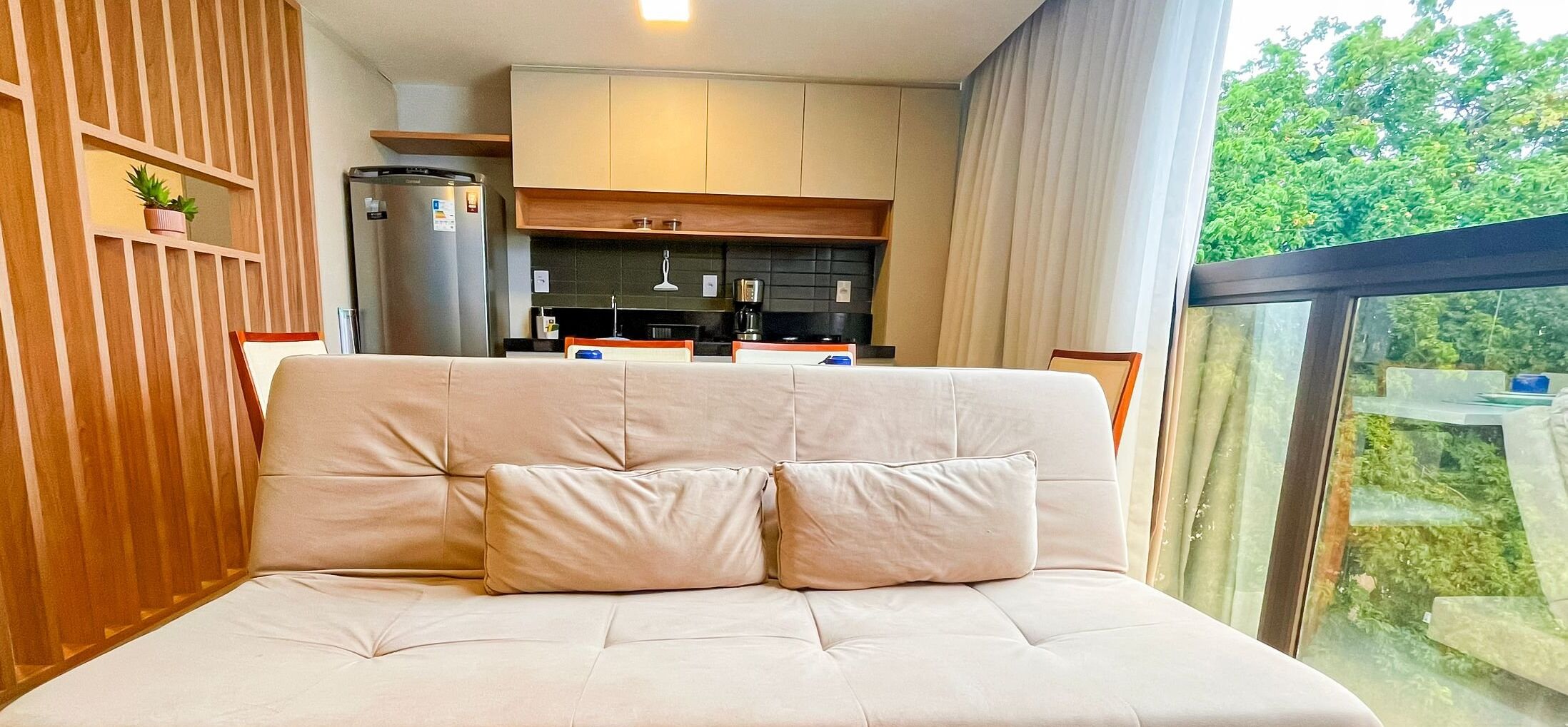 Camera da letto moderna con divano letto, cucina sullo sfondo e vista sul verde.