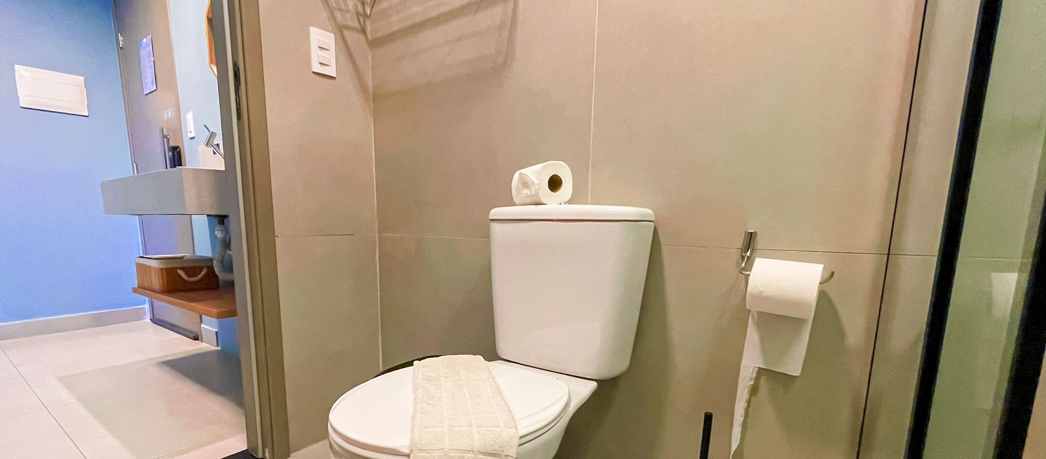 A modern bathroom with a white toilet, a towel on the seat, and a toilet paper holder on the wall.