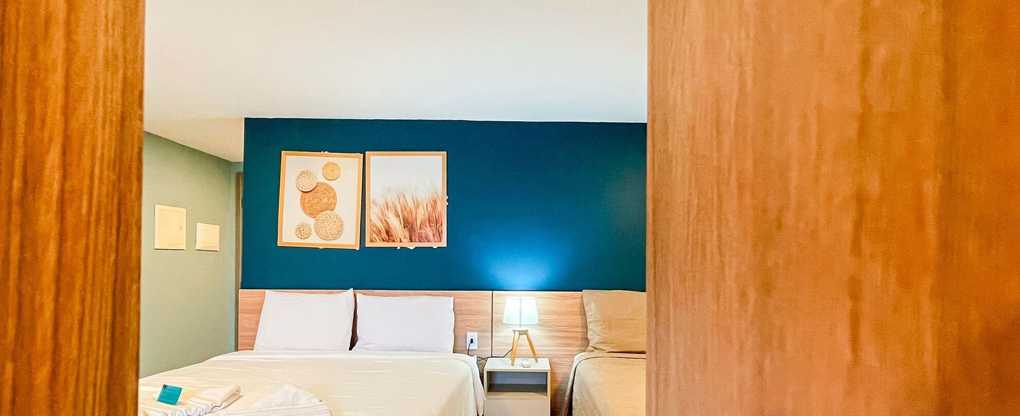 A hotel room with a bed, two bedside tables, a nightstand, and wall art.