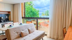 Una habitación de hotel moderna con un ventanal grande, un sofá, un comedor y una kitchenette.