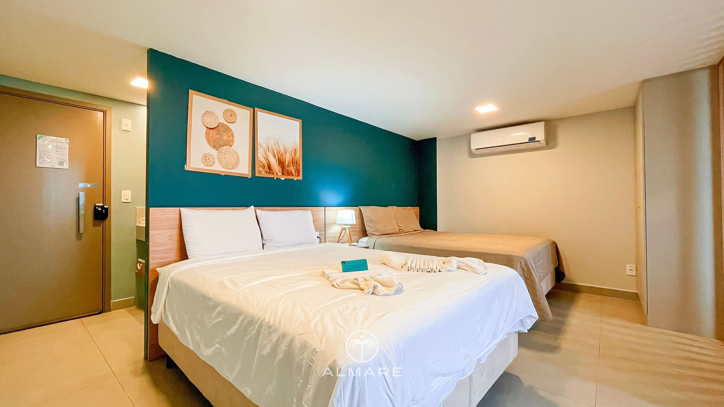Habitación de hotel con una cama grande, una cama más pequeña, un escritorio y aire acondicionado instalado en la pared.