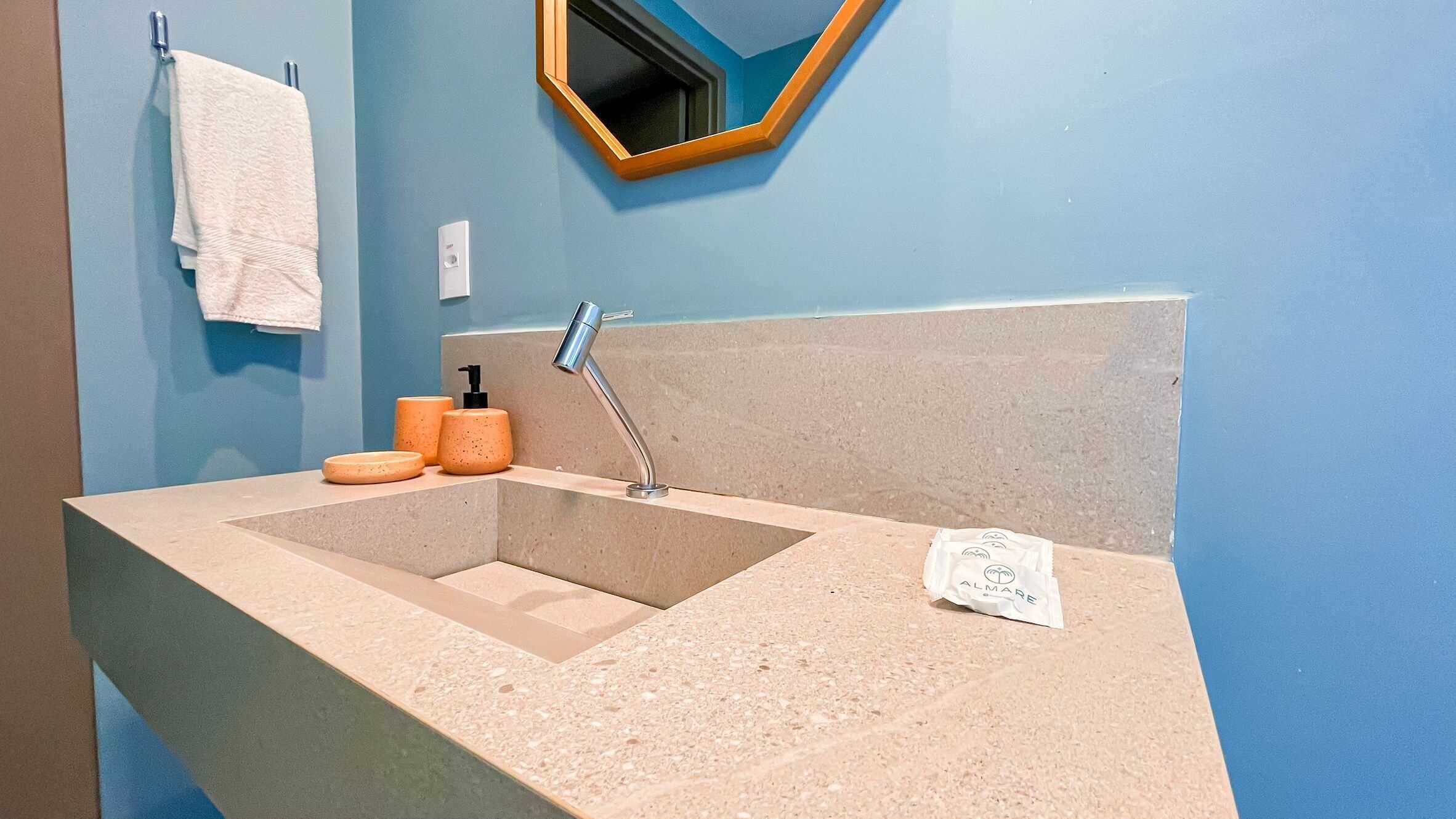 A bathroom with a beige sink, a towel hanging on the wall, and a mirror with a wooden frame.