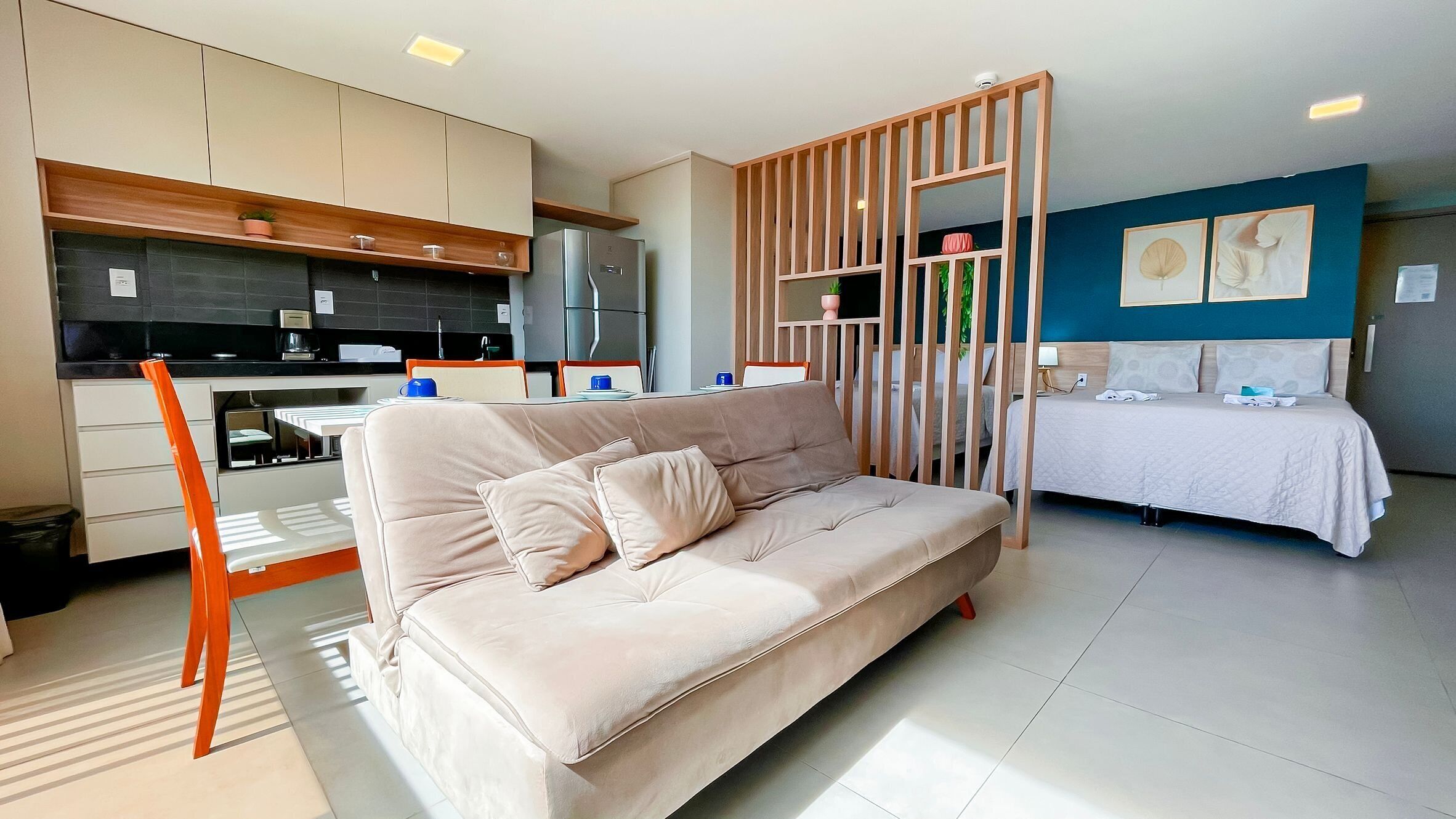 A modern hotel room with a sofa, a dining area, and a kitchen.
