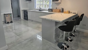A modern kitchen with a central island, bar stools, a microwave, and a toaster. - Mountpanther Holiday House (Downpatrick)