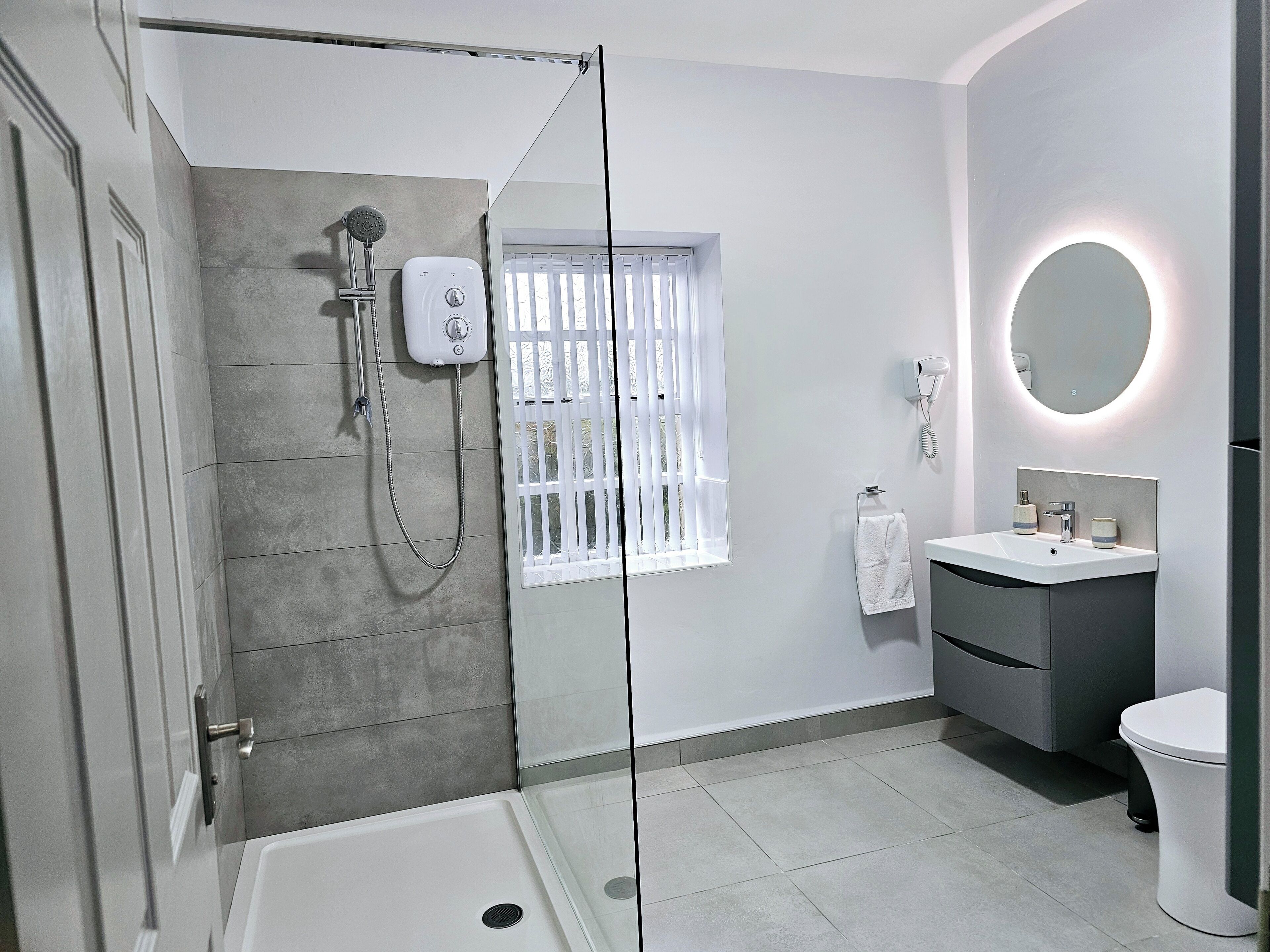 Un baño moderno con ducha de vidrio, un lavabo blanco con espejo redondo y un inodoro.