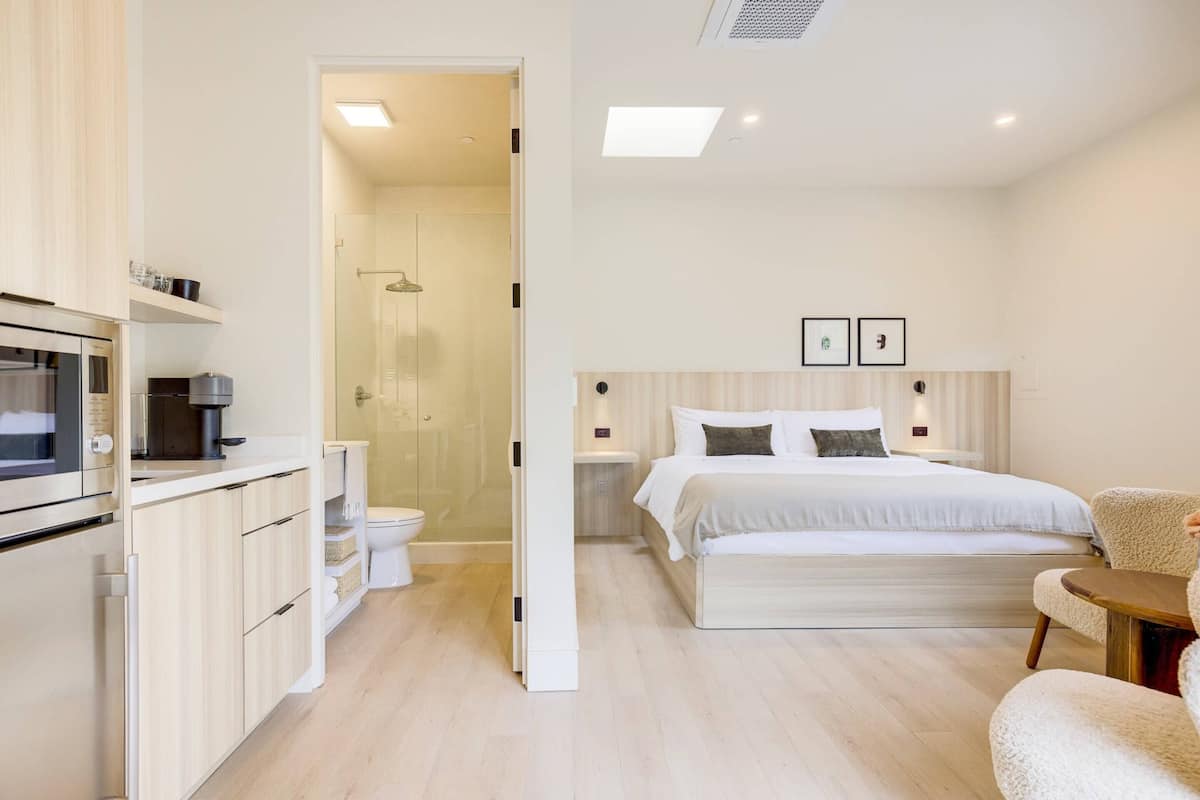 Ein modernes Hotelzimmer mit Küchenzeile, einem großen Bett, einem Nachttisch und einer Duschkabine.