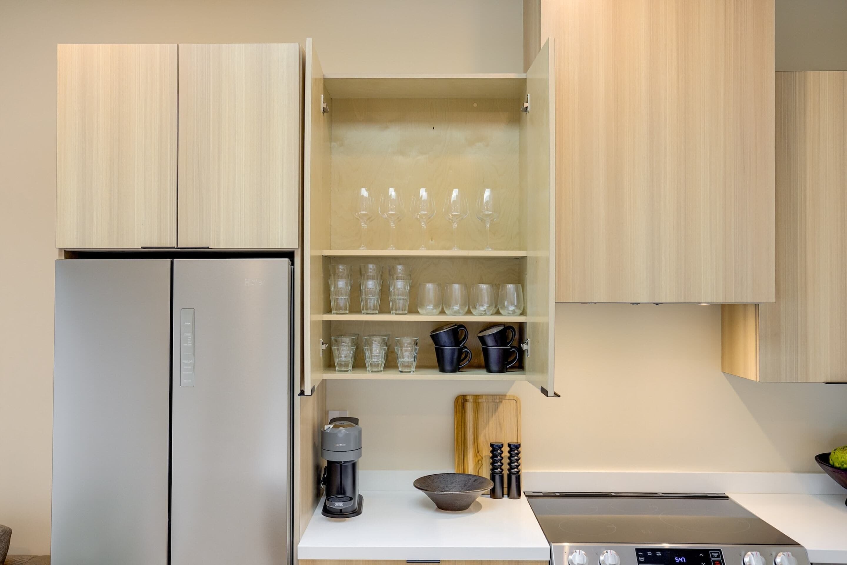 Una cocina moderna con refrigerador integrado, cafetera, tabla de cortar y estufa.