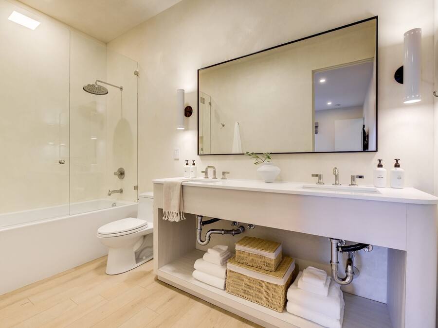 Et moderne badeværelse med en glasafskærmet brusekabine, et hvidt toilet og en vask med et stort spejl.