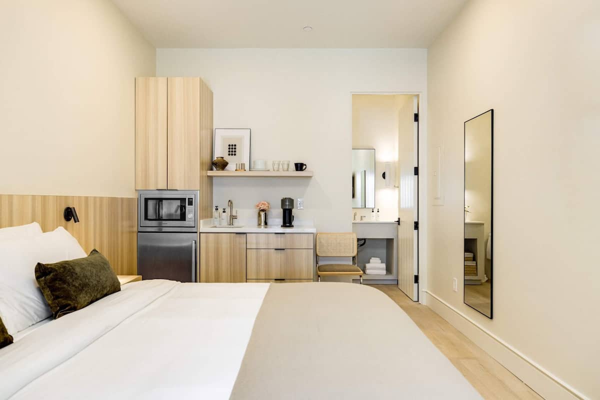 Ein kompaktes Hotelzimmer mit Bett, einer Küchenzeile, einem Spiegel und einer kleinen Sitzecke.