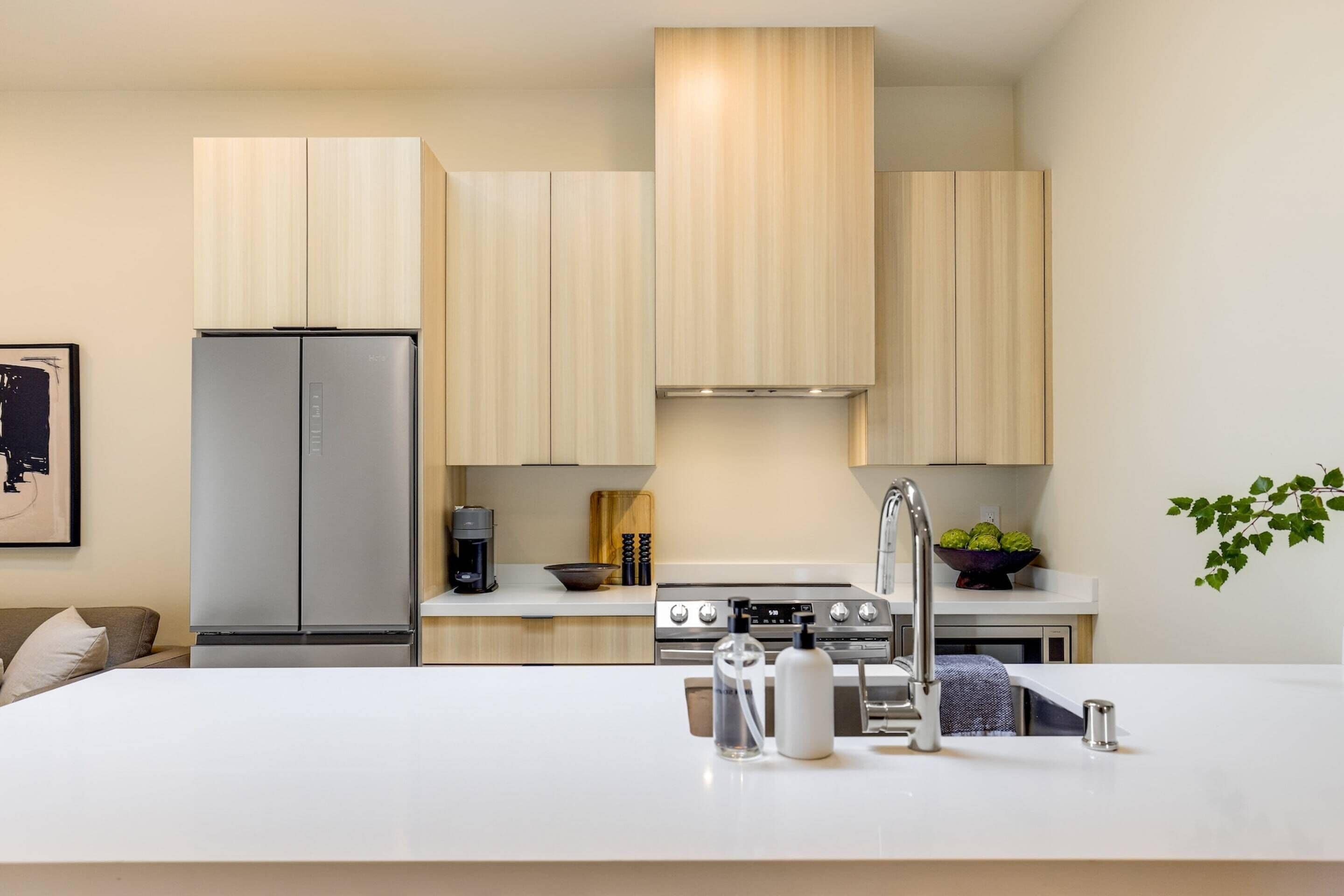 Cocina moderna con armarios de madera clara, electrodomésticos de acero inoxidable y una isla central con pileta y utensilios de bar.
