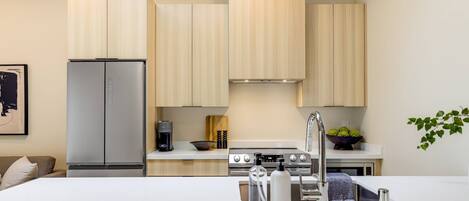 Cocina moderna con armarios de madera clara, electrodomésticos de acero inoxidable y una isla central con pileta y utensilios de bar.