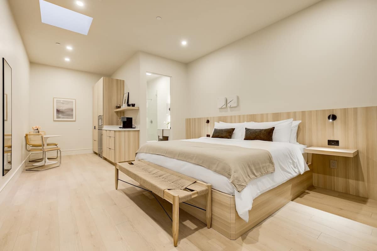 Ein modernes Schlafzimmer mit einem großen Bett, Nachttischen, einer Bank, einem Schreibtisch und einem Stuhl.