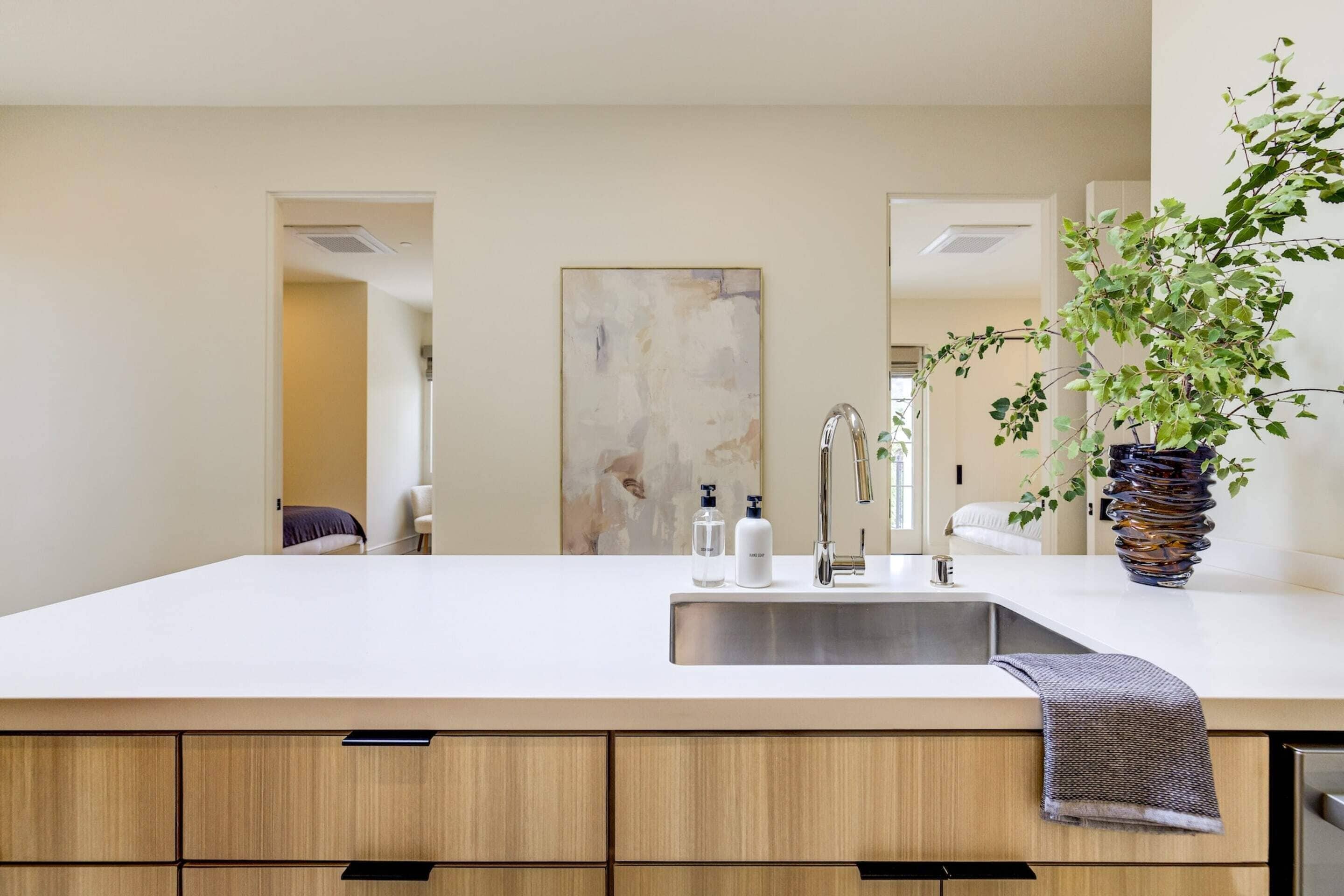 A modern kitchen with a large island, stainless steel sink, and wooden cabinets.