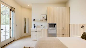 A modern bedroom with a large bed, a built-in wardrobe, a small kitchenette, and a sliding glass door leading to an outdoor area.