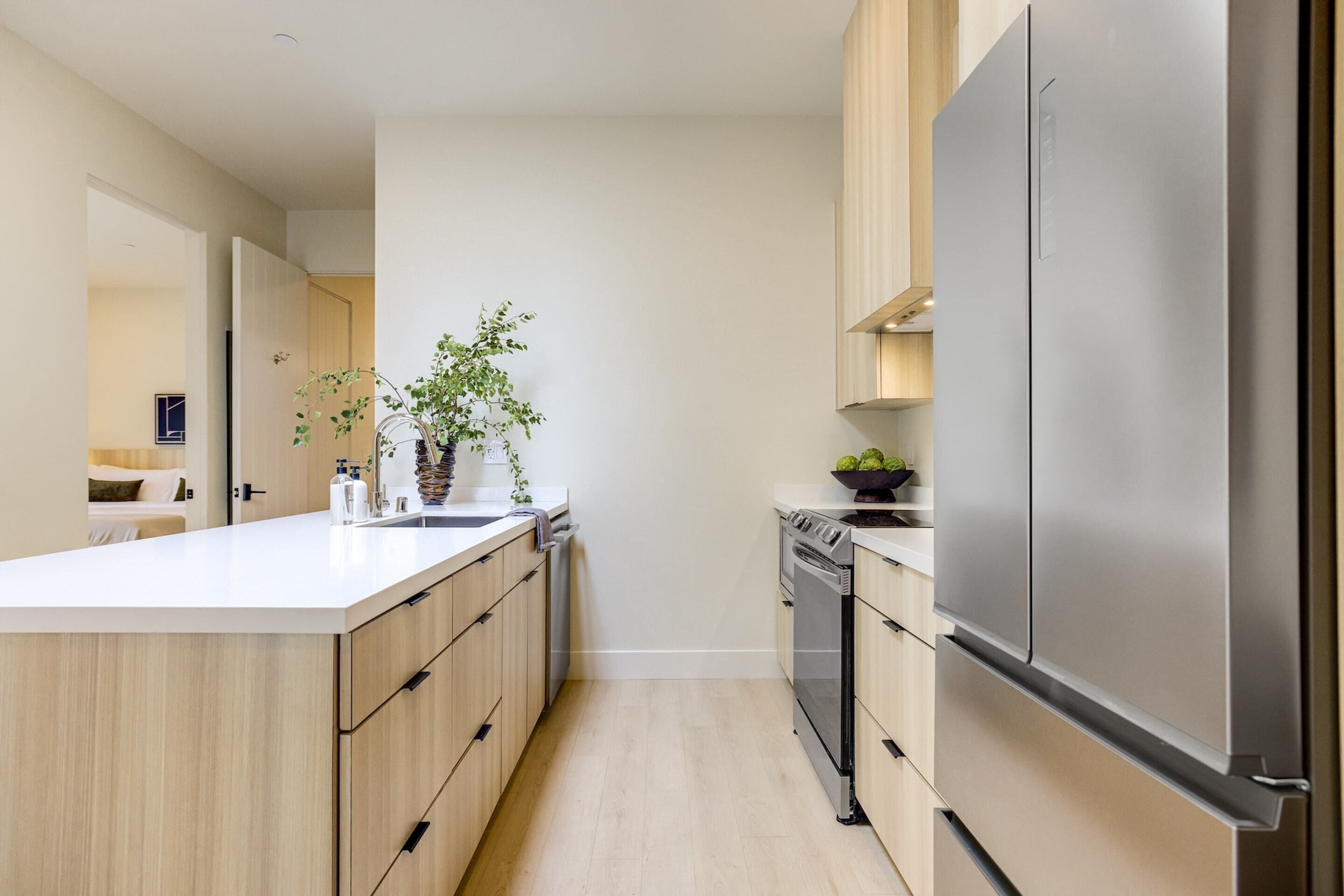 A modern kitchen with a large island, wooden cabinets, stainless steel appliances, and a potted plant.