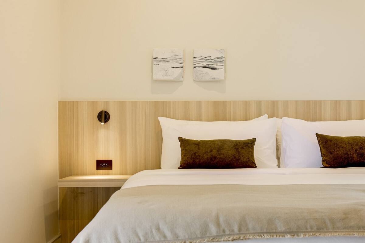 Ein ordentlich bezogenes Bett mit weißen und braunen Kissen, einem hölzernen Kopfteil und zwei an der Wand befestigten Kunstwerken.