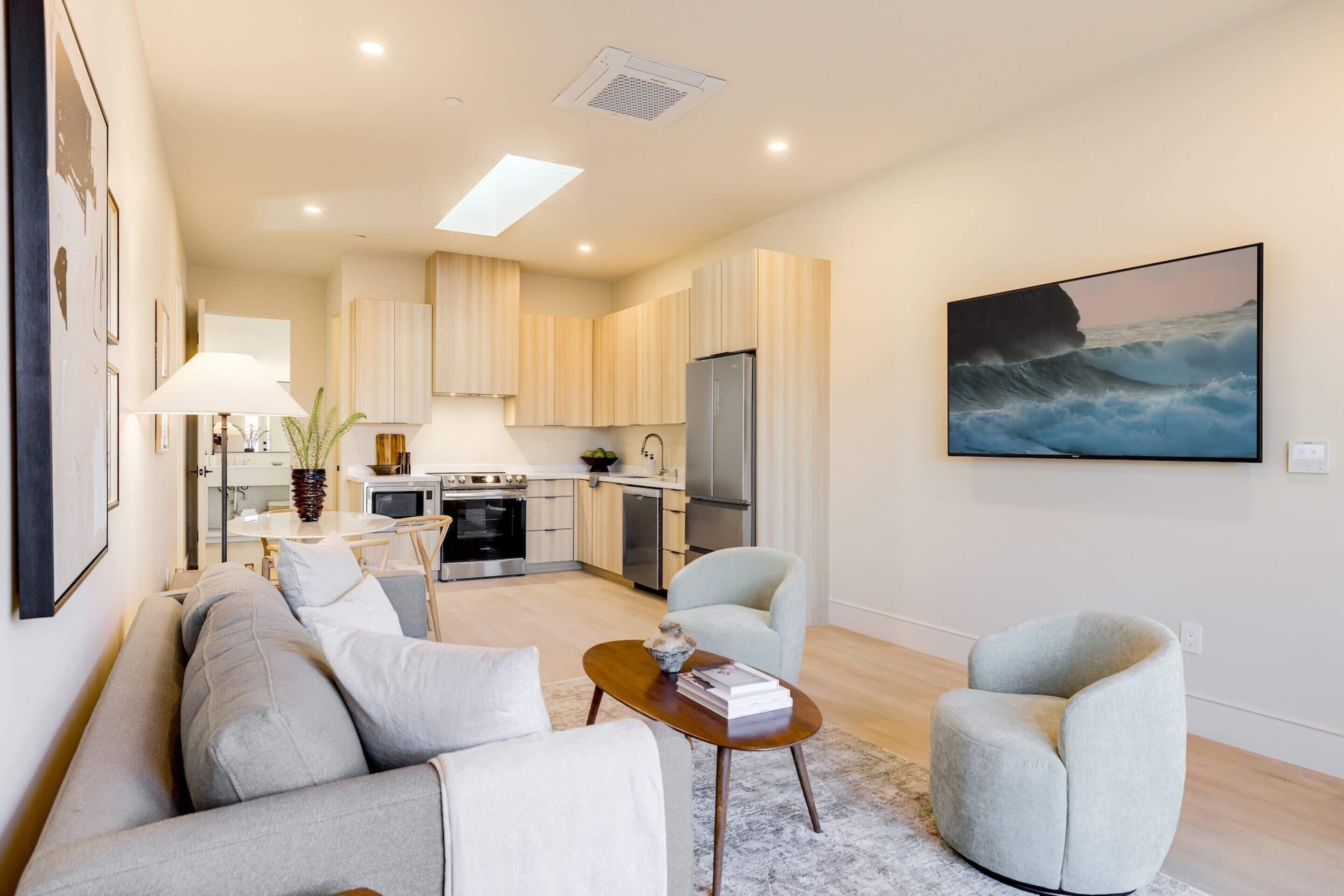 A modern living area with a sofa, armchairs, a coffee table, and a kitchen in the background.