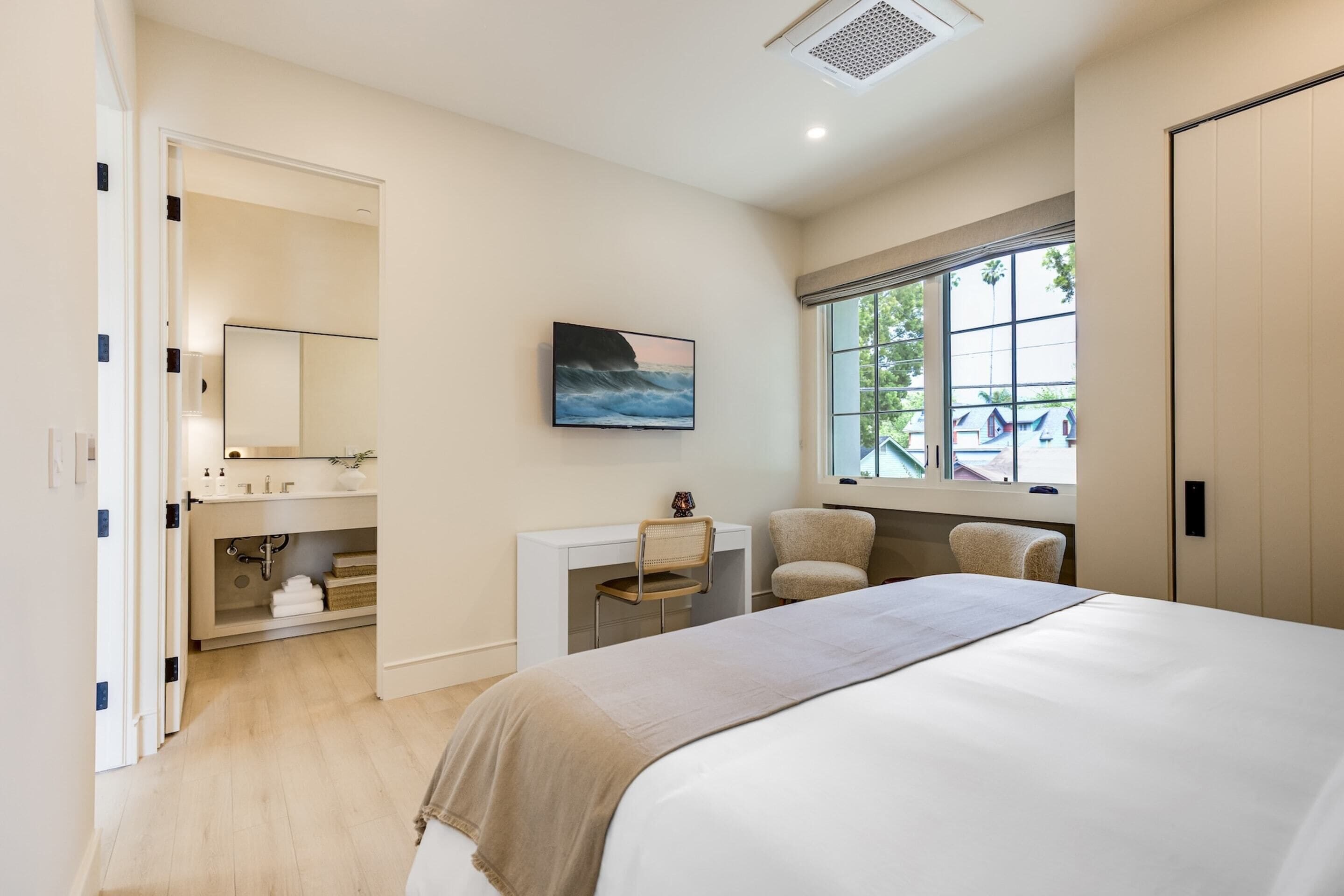 Un dormitorio con cama, escritorio, silla, televisor y ventana.