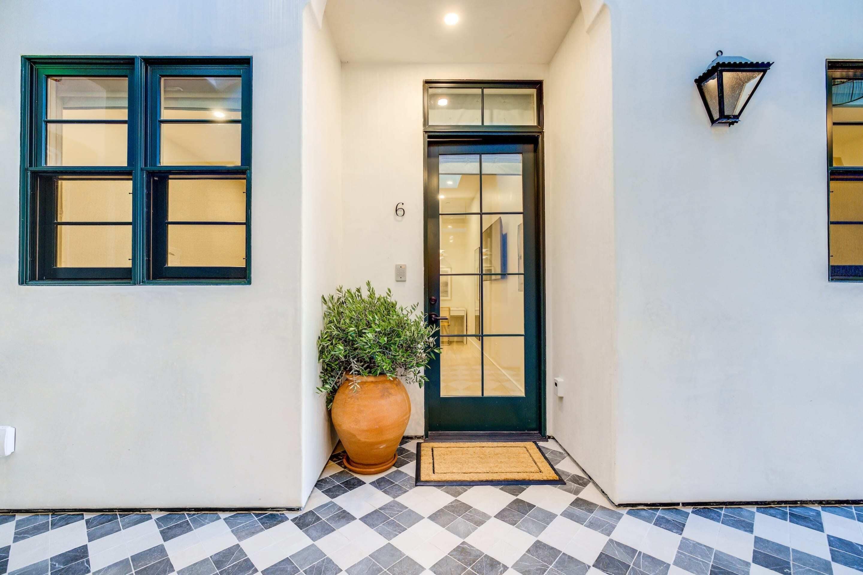 A building entrance with a black door, a potted plant, and a checkered floor.
