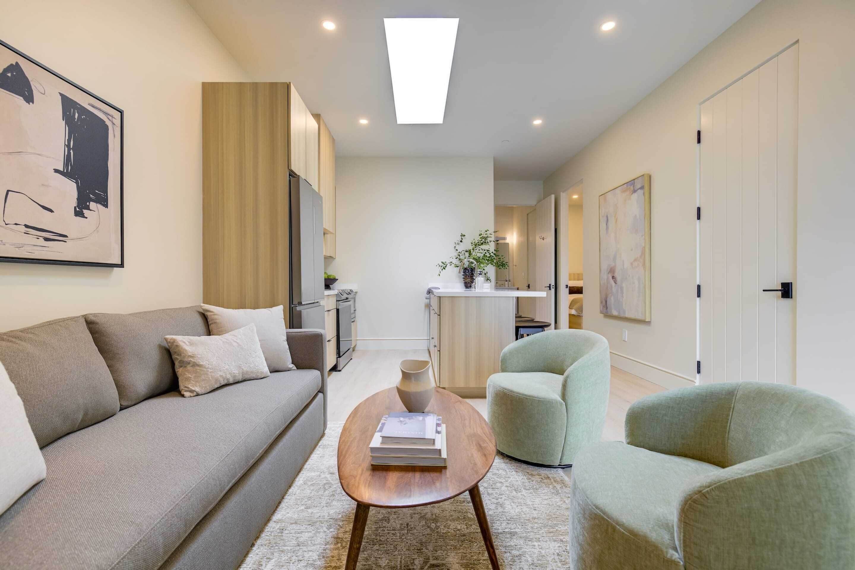 A modern living room with a sofa, a coffee table, and a chair. There is a kitchen area in the background.