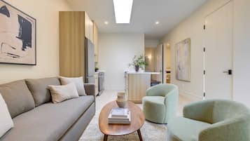 A modern living room with a sofa, a coffee table, and a chair. There is a kitchen area in the background.