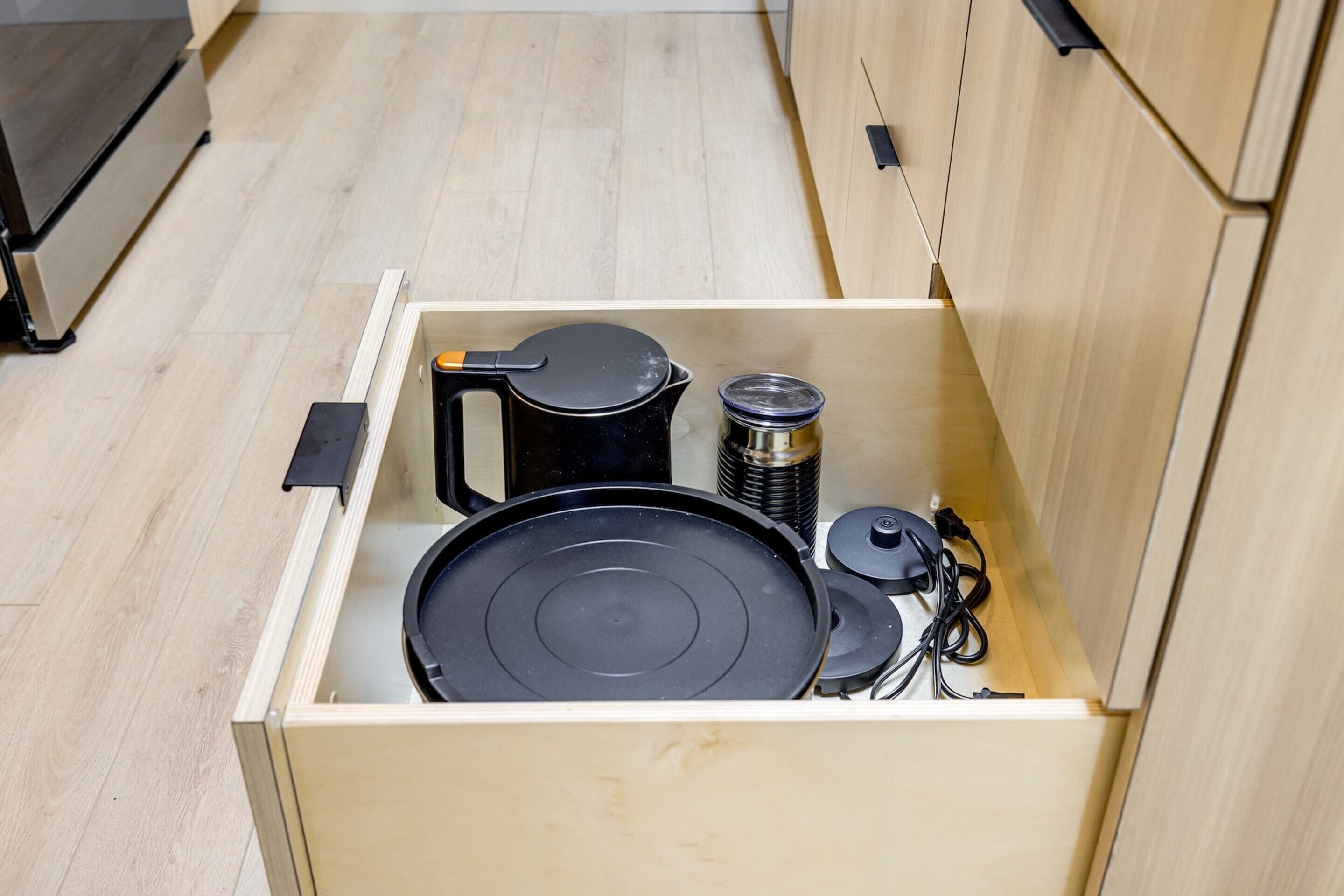 A kitchen drawer with a black frying pan, a coffee pot, and a thermos.