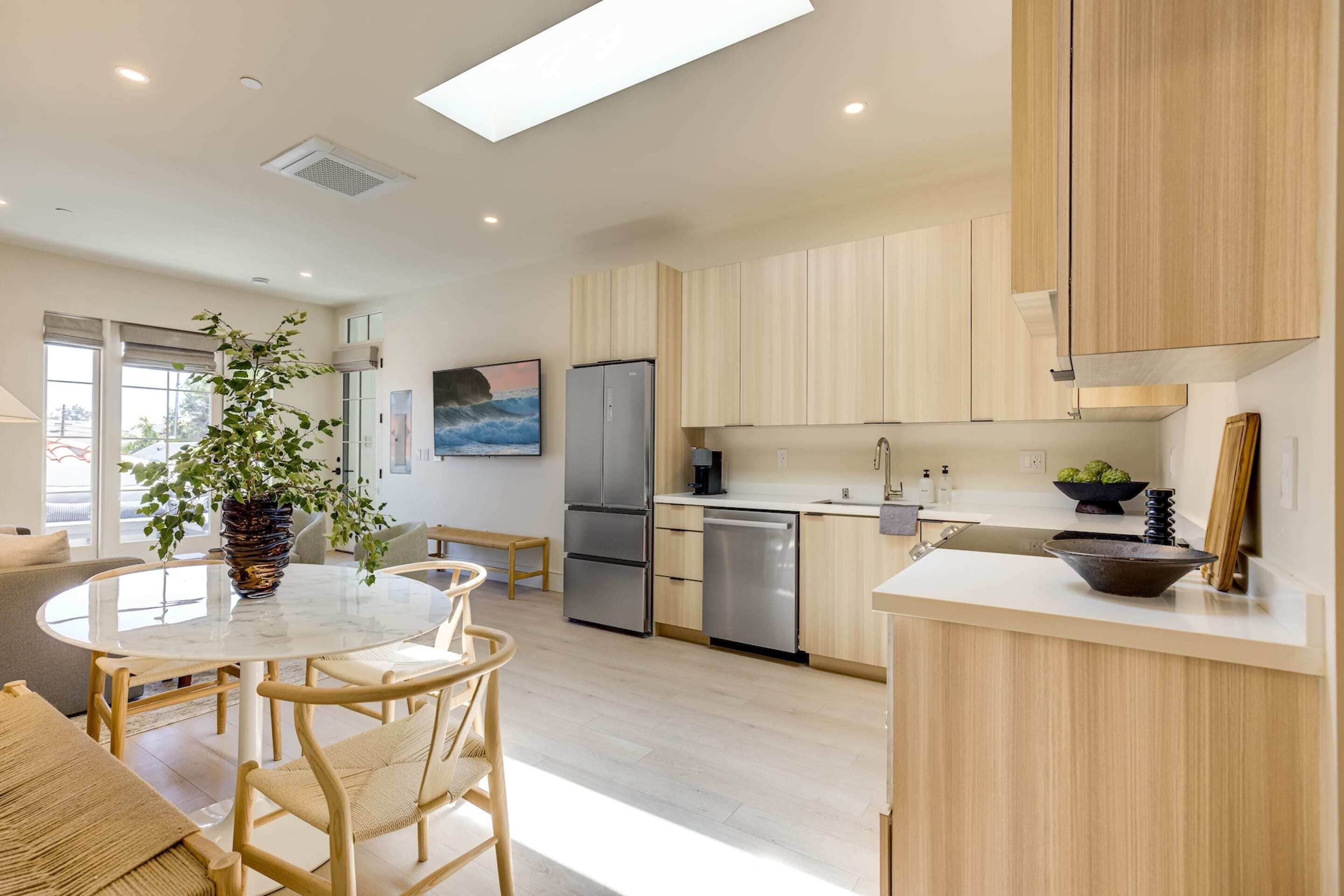 A modern kitchen with light wood cabinets, stainless steel appliances, and a central island with seating.